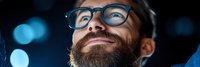 Happy bearded man with glasses looking up with wonder and joy against dark background with blue bokeh lights for inspiration concepts.