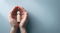 Protective hands cupping wooden figure symbolizing care, support and human protection in healthcare and insurance concepts.