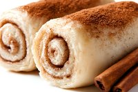 Fresh cinnamon rolls with cream cheese frosting and cinnamon sticks, macro food photography showing swirled pastry details and spice garnish.