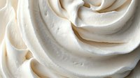 Creamy white whipped frosting swirls in elegant spiral pattern, macro close-up showing soft peaks and smooth texture. Ideal for bakery and dessert designs.