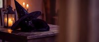 Black cat wearing purple witch hat lying on wooden surface with glowing lantern creating magical Halloween atmosphere for seasonal decorations and spooky celebrations.