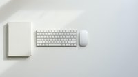 Minimalist white workspace with wireless keyboard, mouse and notebook on clean desk surface for modern office productivity and remote work setup.