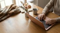 Freelancer working on laptop at wooden desk with coffee mug and dried flowers, cozy home office setup for remote work and productivity projects.