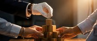 Business professionals collaborating to build wooden block tower symbolizing teamwork, strategy, and corporate growth in warm office lighting.