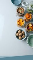 Healthy snacks in glass jars and bowls with nuts, dried fruits, energy balls and seeds arranged on clean kitchen counter for meal prep storage.