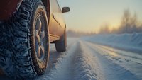 Close-up view of off-road tire on snowy winter road during sunset, showing deep tread pattern and vehicle tracks in fresh snow on rural path.