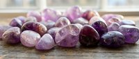 Collection of polished amethyst gemstones in various purple shades scattered on wooden surface for jewelry making, crystal healing and decorative purposes.