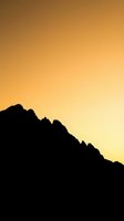 Silhouette of jagged mountain ridge against warm golden sunset sky, creating dramatic contrast for nature and travel backgrounds.