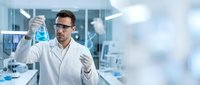 Male scientist in white lab coat examining blue liquid in glass flask during laboratory research experiment with modern equipment background.