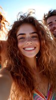 Happy young woman with curly hair taking selfie with friends on sunny beach day. Joyful summer vacation moments with genuine smile and carefree attitude.