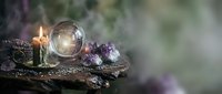 Mystical fortune telling setup with crystal ball, burning candle and amethyst stones on wooden surface for divination and spiritual practices.