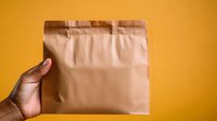 Hand holding brown kraft paper mailing envelope against vibrant yellow background, demonstrating secure packaging for shipping and delivery services.
