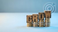 Wooden letter blocks spelling GROW on ascending coin stacks representing financial growth, investment success and business development concept.