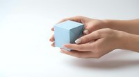 Female hands gently holding light blue geometric cube on white background. Minimalist concept for protection, care, and precious objects.