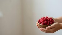 Close-up of hands holding a wooden bowl filled with fresh red raspberries against a neutral background. Suitable for food, nutrition, and healthy lifestyle content.