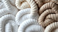 Soft twisted cotton rope in white and beige colors creating abstract curved lines and patterns. Natural fiber texture background for design and decoration.