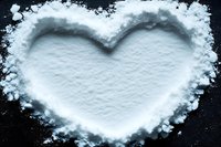 Heart shape made from white flour powder on dark surface for baking and cooking concepts.