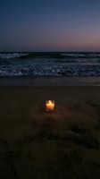Glowing candle on sandy beach at twilight with ocean waves and starry purple sky creating peaceful romantic atmosphere for meditation and relaxation.
