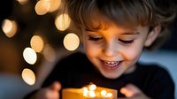 Young Caucasian boy with blonde hair smiling joyfully while holding warm glowing lights in cupped hands against bokeh background for holiday magic concepts.