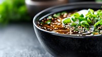 Asian noodle soup with sesame seeds and fresh herbs in black bowl, traditional comfort food for restaurant menu and culinary content.