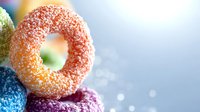 Colorful sugar-coated gummy candy rings stacked in vibrant blue, orange, and purple colors against blurred bokeh background, macro food photography.