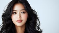 Young Asian woman with flowing black hair and natural makeup against light background, professional beauty portrait showcasing glowing skin and soft expression.