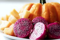 Fresh sliced watermelon radish with vibrant magenta interior displayed alongside chunks of orange cantaloupe and pumpkin on white plate, macro food photography.