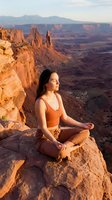 Young woman practicing meditation yoga on red rock cliff edge overlooking desert canyon landscape at golden hour sunrise creating peaceful mindfulness moment.