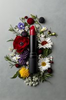 Red lipstick surrounded by fresh flowers and berries on gray background. Floral cosmetic flatlay composition with daisies, anemones and wildflowers.