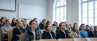 Diverse group of university students sitting in modern lecture hall during academic seminar or conference presentation.