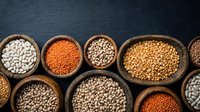 Assorted legumes and pulses in wooden bowls including lentils, chickpeas, and beans on dark surface for cooking and nutrition content.
