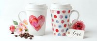 Watercolor heart and polka dot ceramic mugs with lids, surrounded by fresh roses, coffee beans, and love tag on white background for beverage branding.