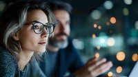 Young Caucasian businesswoman wearing glasses looks thoughtfully into distance during evening office meeting, bokeh lights create professional atmosphere.