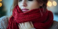 Young woman wearing cozy red knitted scarf and beige sweater against blurred bokeh lights background, winter fashion portrait with soft dreamy atmosphere.