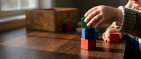 Young child stacking colorful wooden building blocks on a wooden table, learning through creative play and early childhood development.