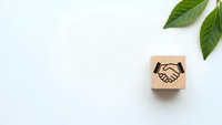 Wooden cube with handshake symbol and green leaves on white background representing business partnership, cooperation and sustainable growth concepts.