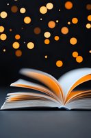Open book with pages fanned out against dark background with magical glowing orange bokeh lights floating above, creating dreamy atmospheric reading scene.