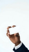 Close-up of male hand with dark skin tone holding blank white business card against neutral background. Suitable for corporate branding, contact information, and professional marketing materials.