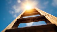 Wooden ladder reaching towards bright sun against blue sky, low angle view capturing aspirational journey upward and achievement concept for business success.