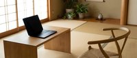 Modern minimalist home office with laptop on wooden desk and chair in Japanese-style room with tatami flooring and natural lighting for remote work.