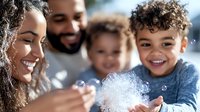 Young mixed race family playing with soap bubbles outdoors, enjoying sunny day together. Joyful lifestyle moment capturing genuine happiness and connection.