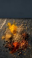 Assorted spices including turmeric powder, cumin seeds, coriander, star anise, and peppercorns arranged on dark slate surface for culinary and cooking projects.