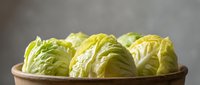 Fresh napa cabbage heads in wooden bowl on neutral background for healthy cooking and Asian cuisine recipes.