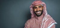Confident Middle Eastern man in traditional red and white keffiyeh and thobe smiling against dark gray background.