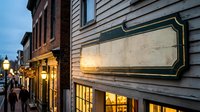 Historic colonial street at dusk with vintage wooden buildings, warm glowing windows and blank antique signage ready for custom text or branding design.