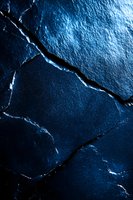 Dark blue cracked stone surface with dramatic lighting creates abstract pattern of lines and textures, highlighting natural geological formations in deep shadows.