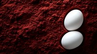 White chicken eggs on rich red paprika powder background, creating striking color contrast for food photography and culinary concepts.