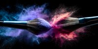 Makeup brushes colliding with explosion of colorful powder in blue, purple and pink hues against black background. Cosmetic art concept.