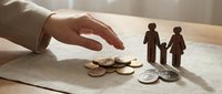 Protective hand gesture over wooden family figures and coins symbolizing financial security, insurance coverage, and wealth protection for loved ones.