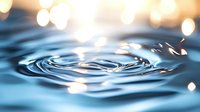 Water drop creating concentric ripples on blue surface with soft bokeh lights in background, macro photography capturing liquid motion and tranquil aquatic patterns.